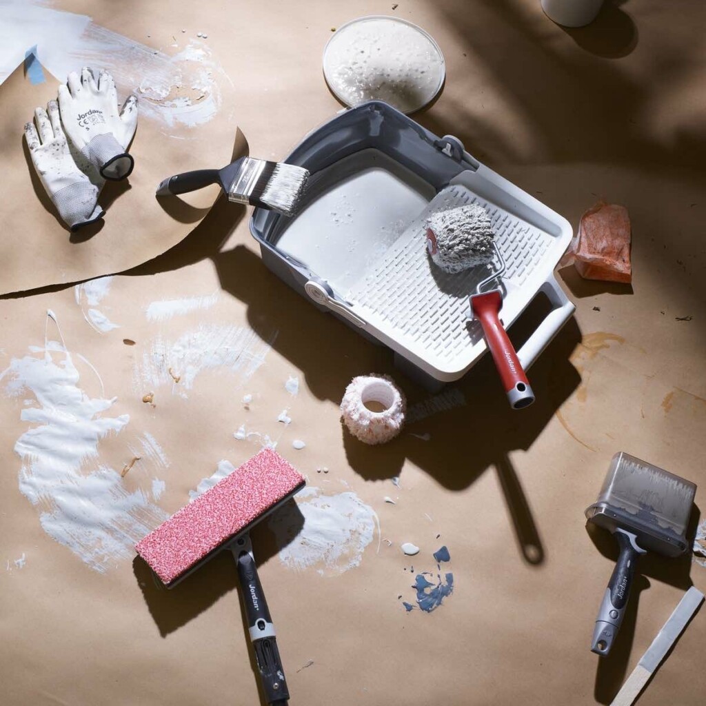 Malekoster og maleutstyr som ligger på gulv dekket i papir