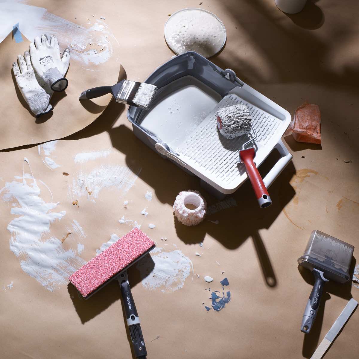 Malekoster og maleutstyr som ligger på gulv dekket i papir