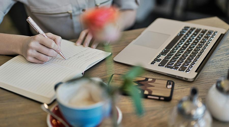 Person som sitter ovenfor en notatblokk og en pc.