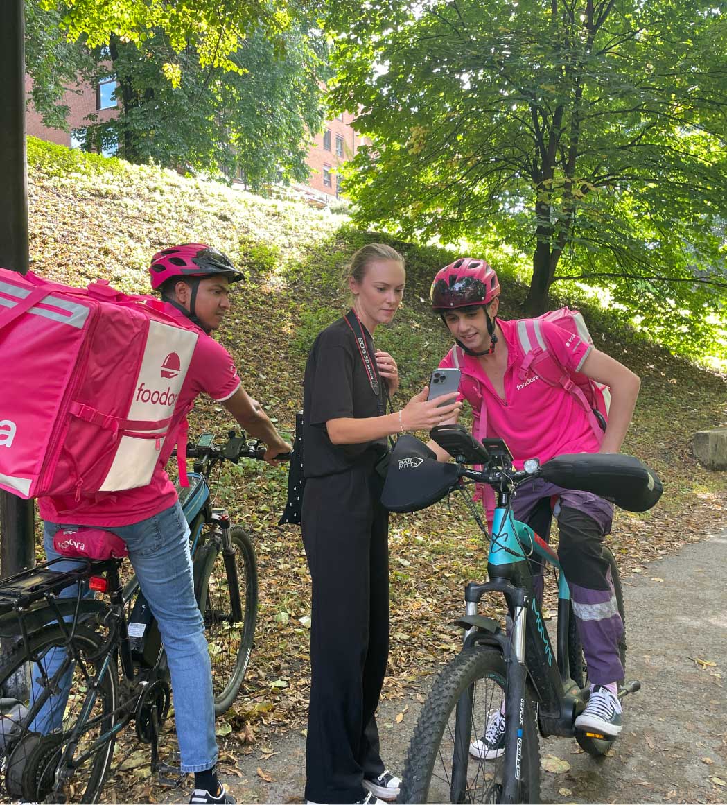To foodora syklister er ute og ser på bilder på telefonen til fotografen, under produksjonsdagen.